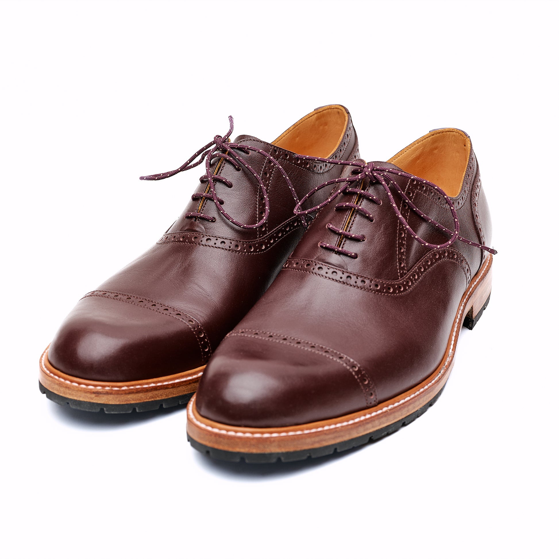 Pair of brown leather Oxford shoes with brown soles on white background. 