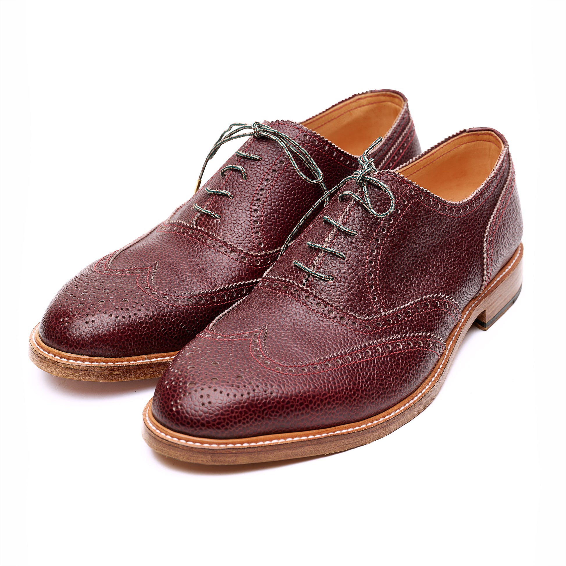Pair of textured brown leather brogue Oxford shoes with brown soles on white background. 
