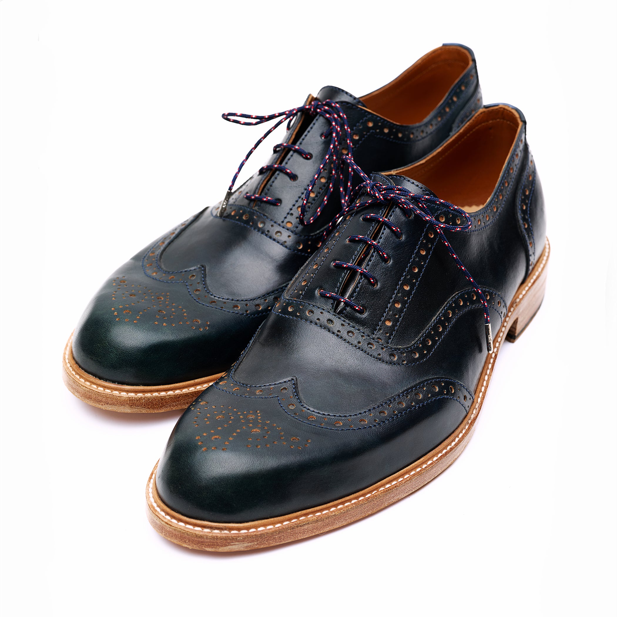Pair of black leather brogue Oxford shoes with brown soles on white background. 