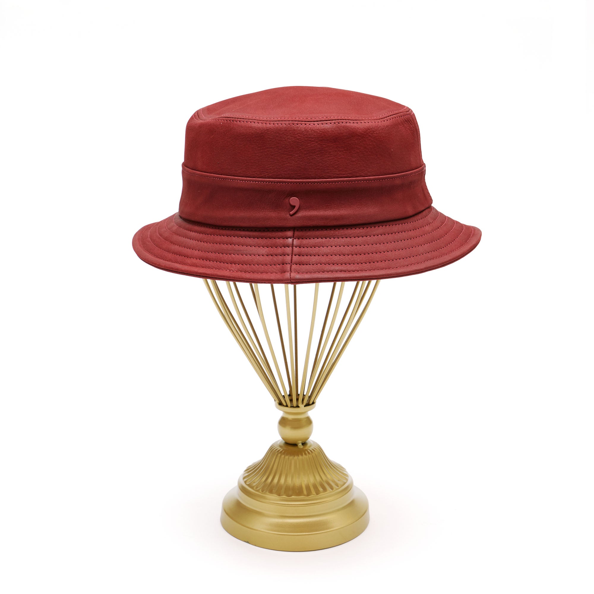 Red leather bucket hat on gold hat stand in front of white background. 