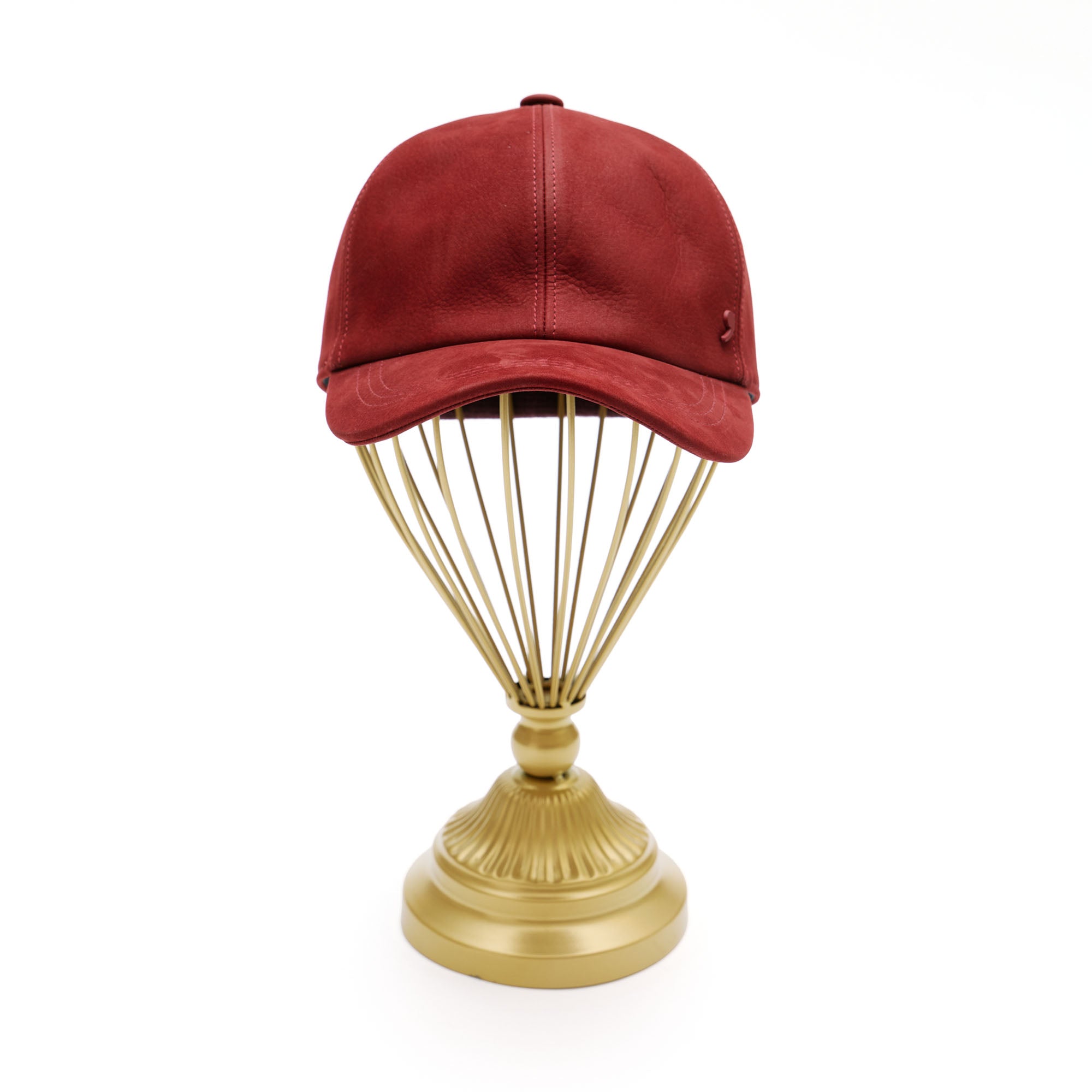 Red suede baseball cap on gold hat stand in front of white background. 