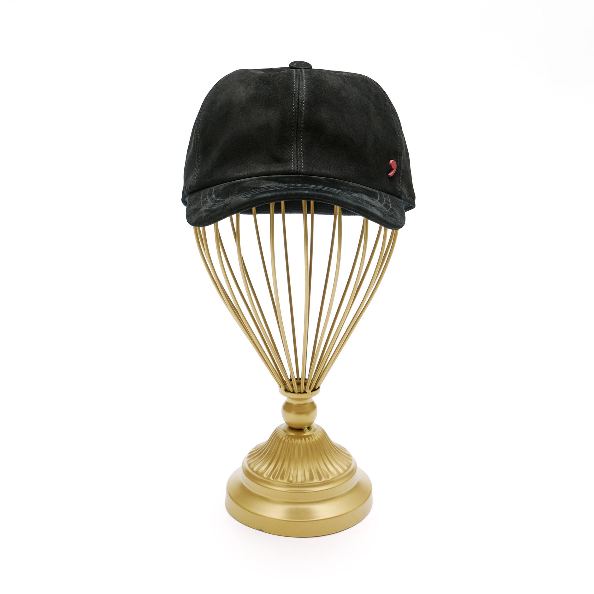 Black suede baseball cap on gold hat stand in front of white background. 