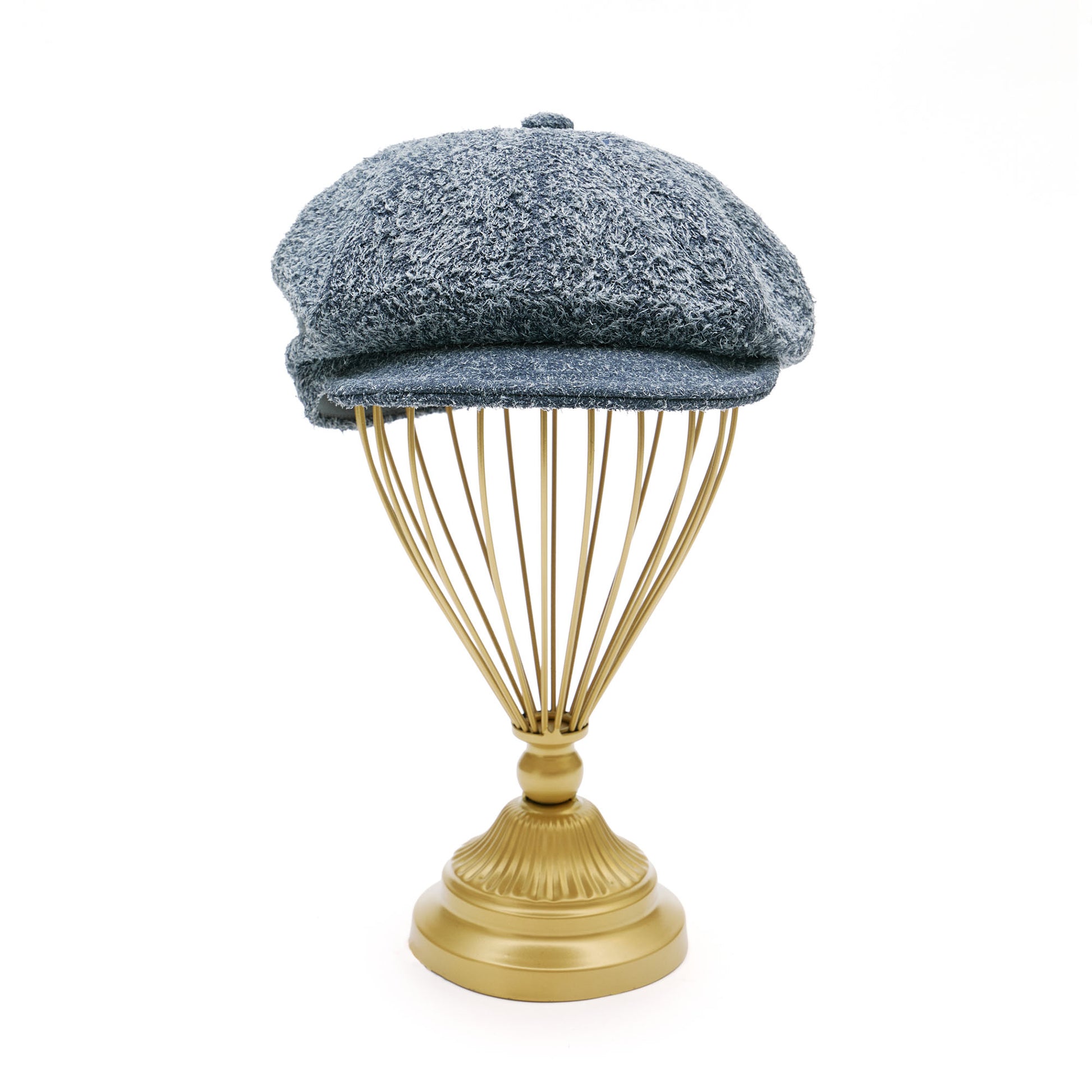 Grey suede melton cap on  gold hat stand in front of white background. 