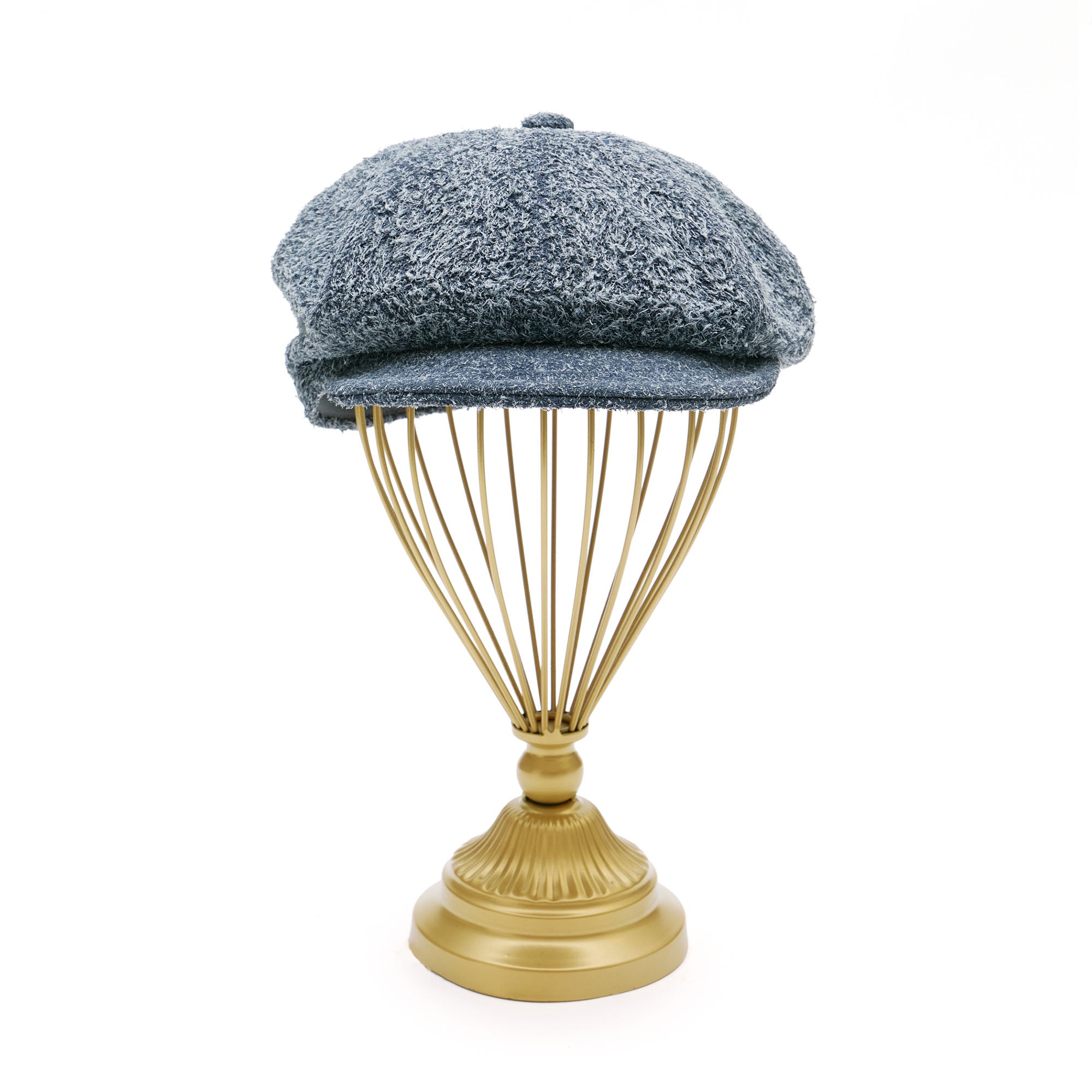 Grey suede melton cap on  gold hat stand in front of white background. 