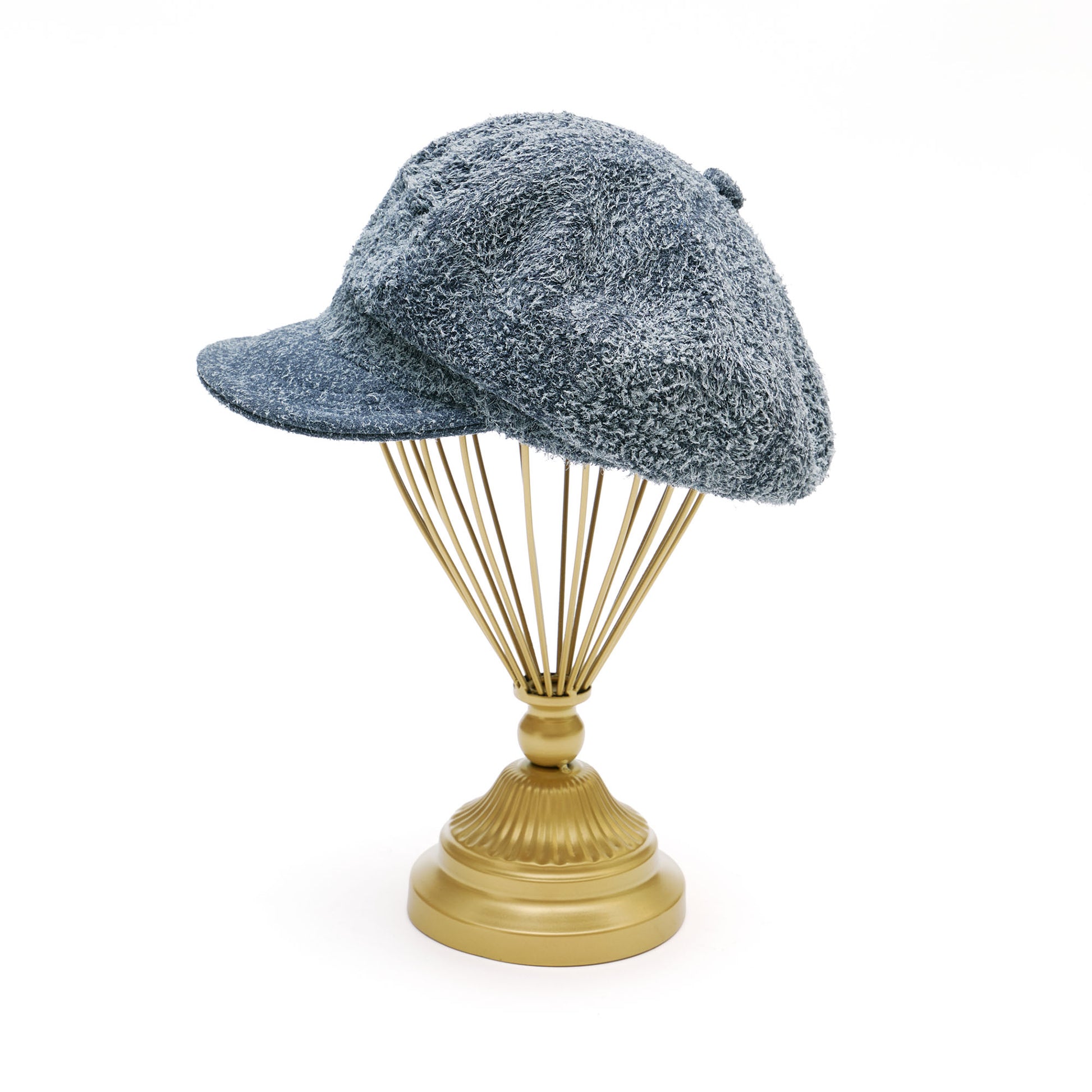 Grey suede melton cap on  gold hat stand in front of white background. 