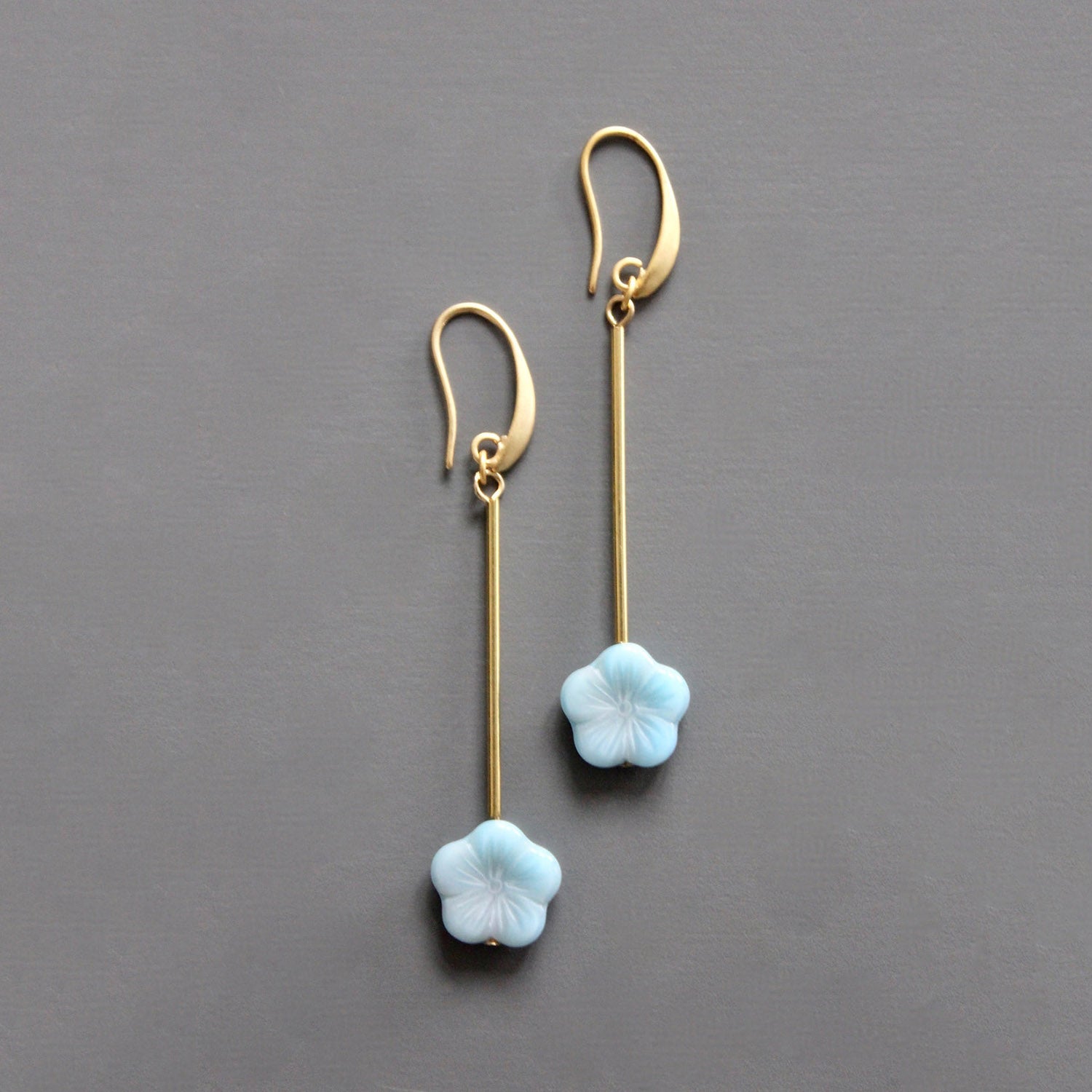 Brass earrings with light blue flower-shaped charms on a gray background