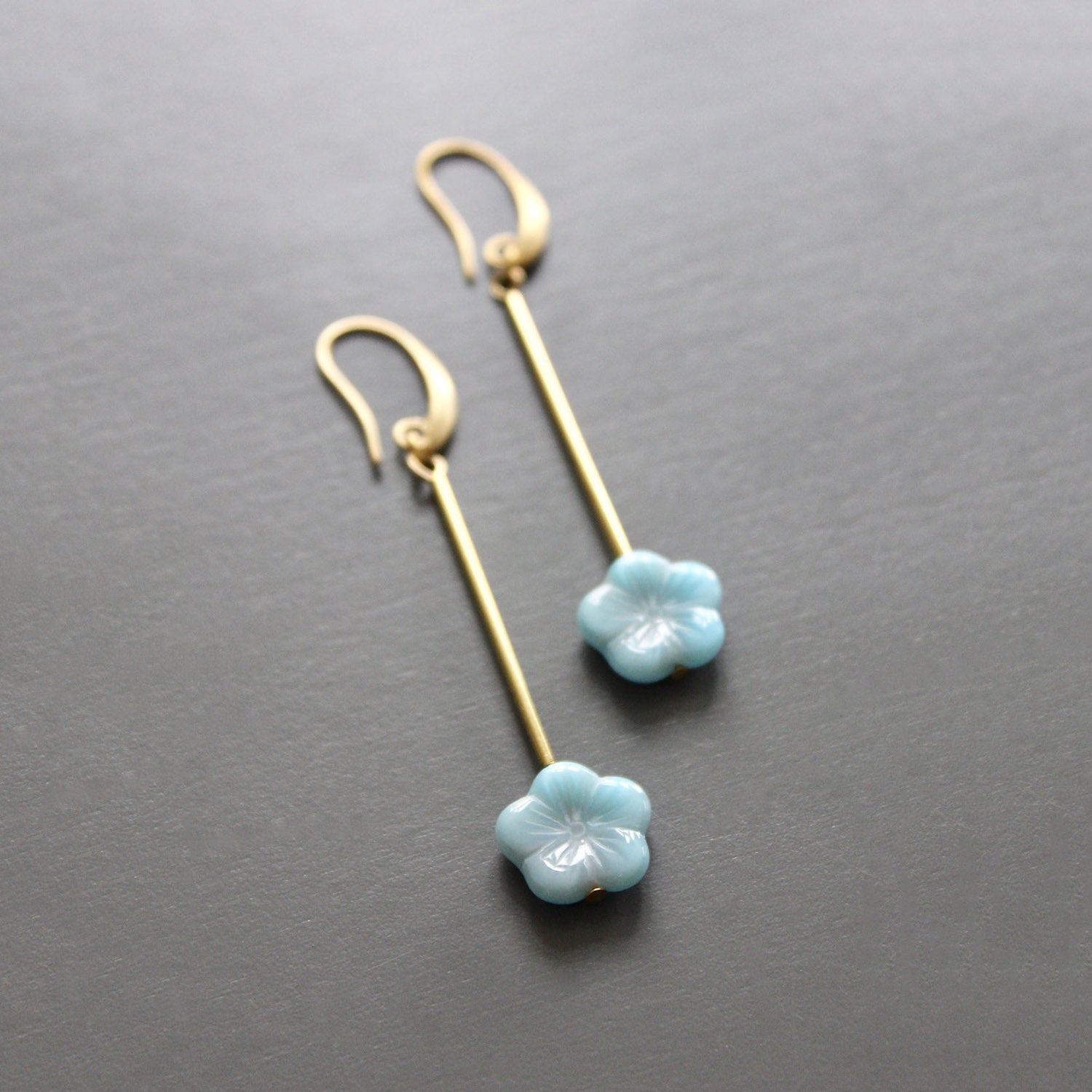 Brass earrings with light blue flower-shaped charms on a gray background.