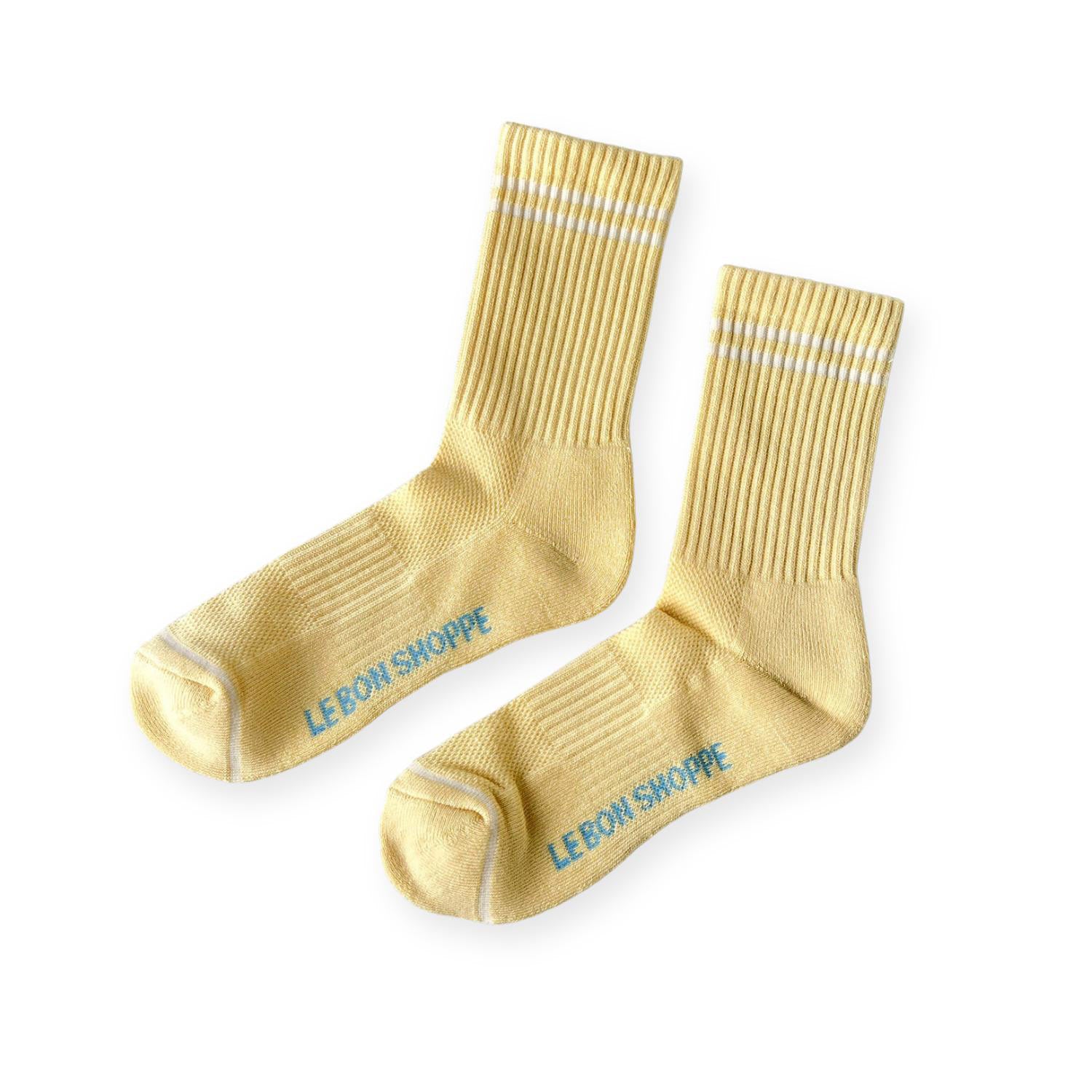 Pair of light yellow ribbed sport socks with double white stripe around ankle and "Le Bon Shoppe" on soul. 