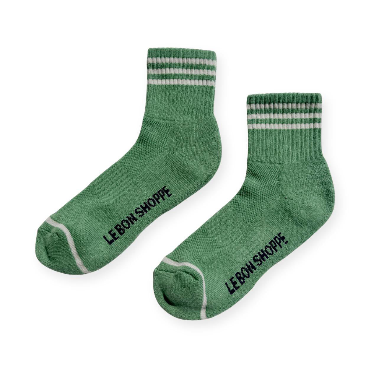 Pair of green sport socks with white stripes on ankle and Le Bon Shoppe text on soul. 