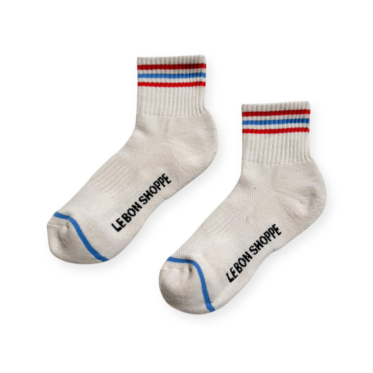 Pair of white sport socks with red and blue stripes on ankle and Le Bon Shoppe text on soul. 