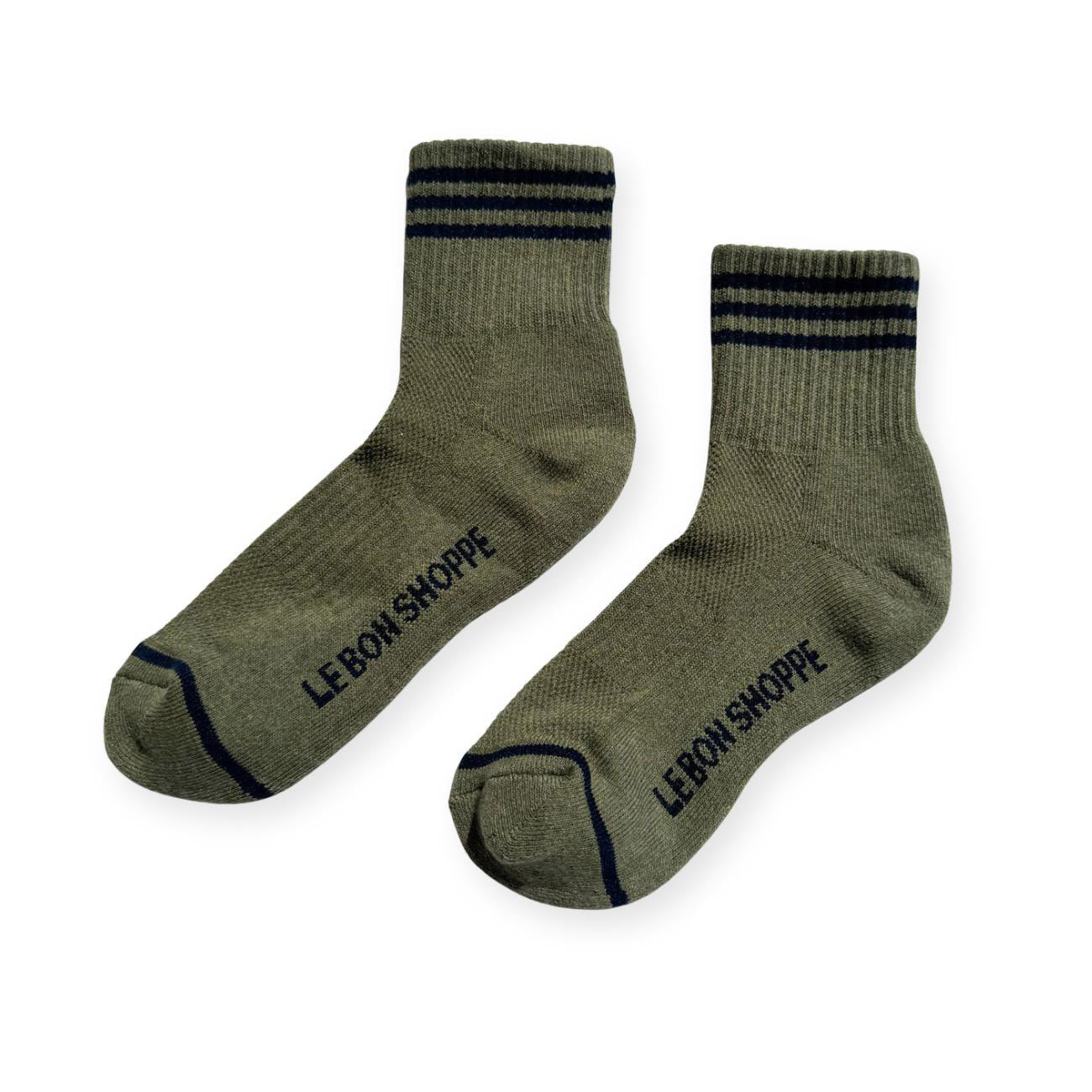 Pair of sage green sport socks with black stripes on ankle and Le Bon Shoppe text on soul. 