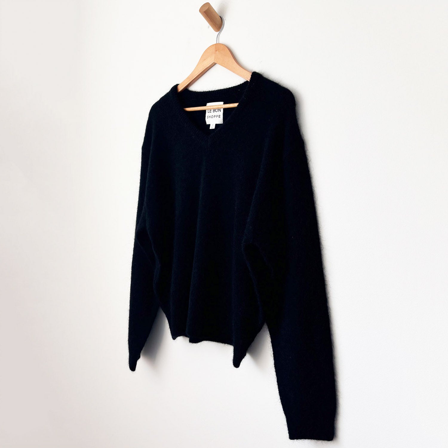 Black mohair sweater hanging on wood hanger in front of white wall. 