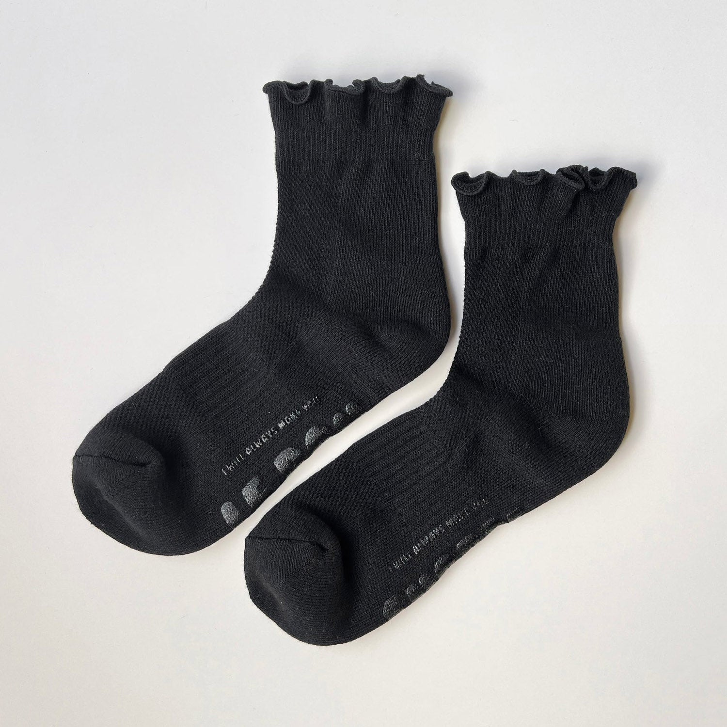Black ruffle top socks with black text on sole on grey background. 