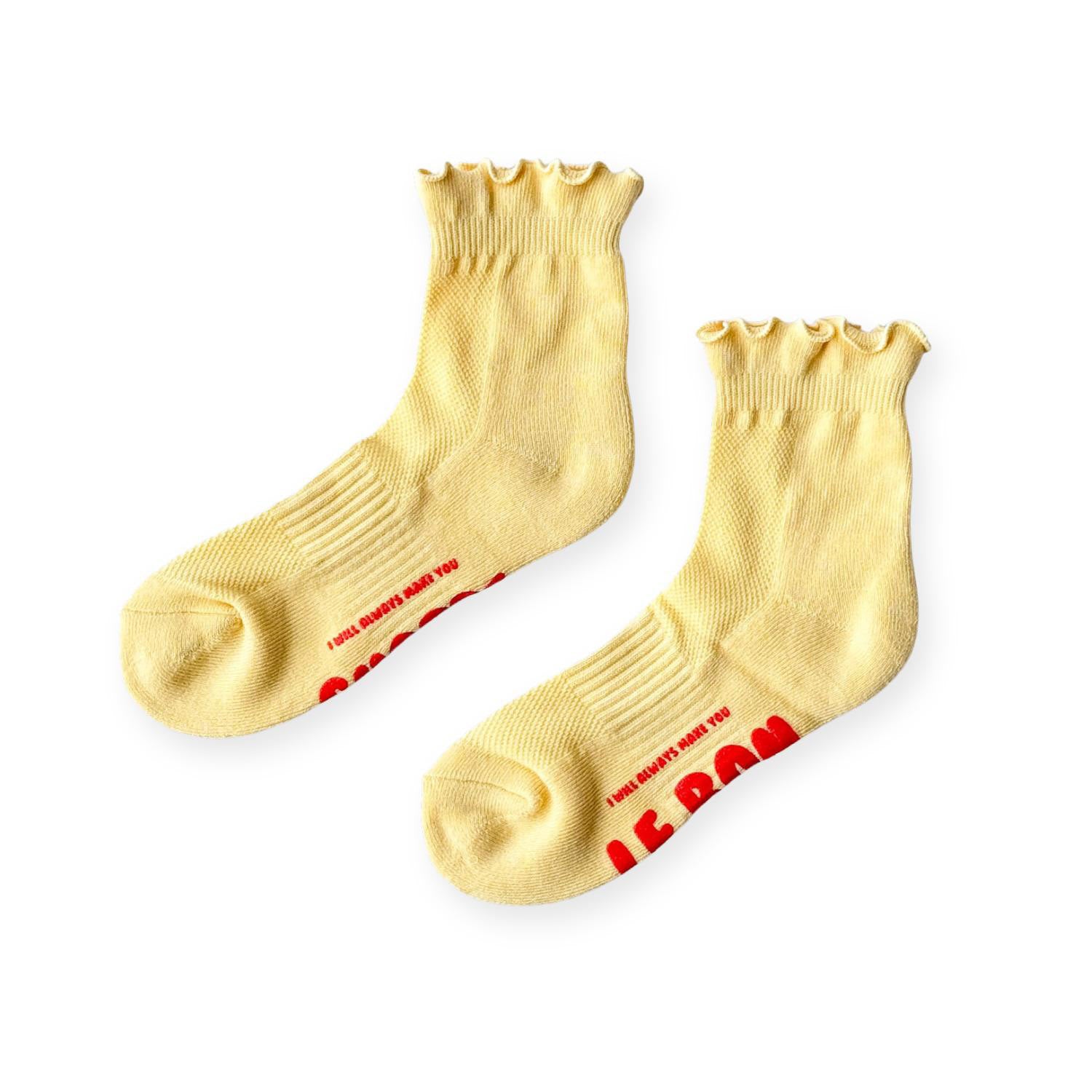 Yellow ruffle top socks with red text on sole on grey background. 