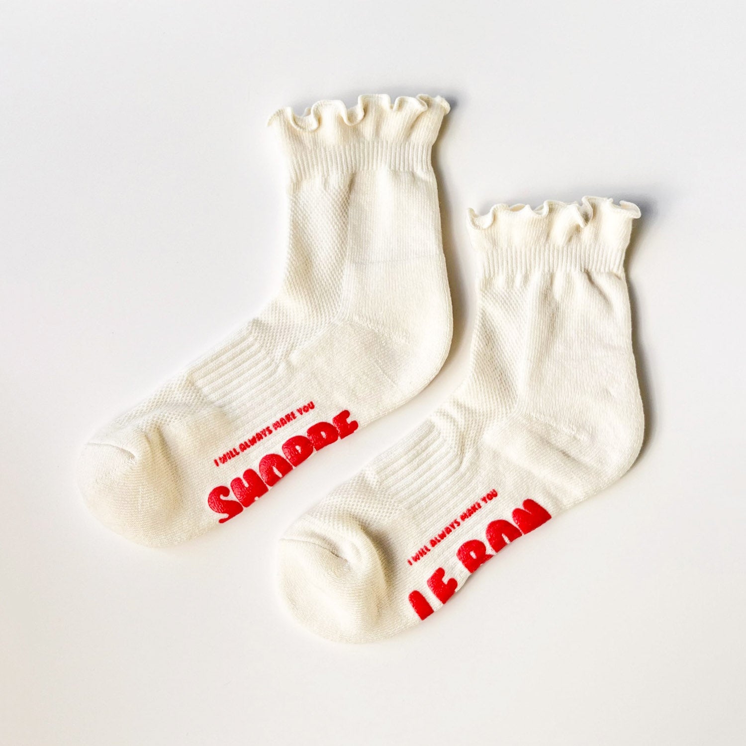 White ruffle top socks with red text on sole on grey background. 