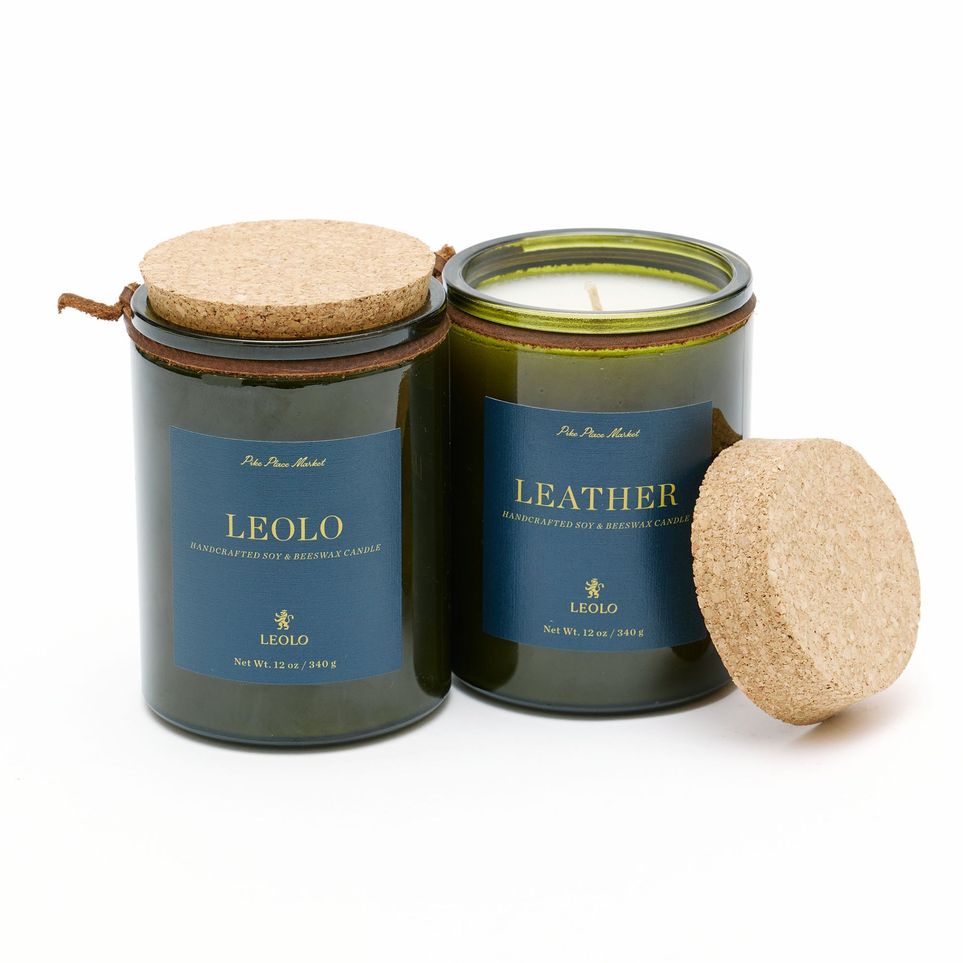 Two candles in green glass jars with cork lists, against white background. 