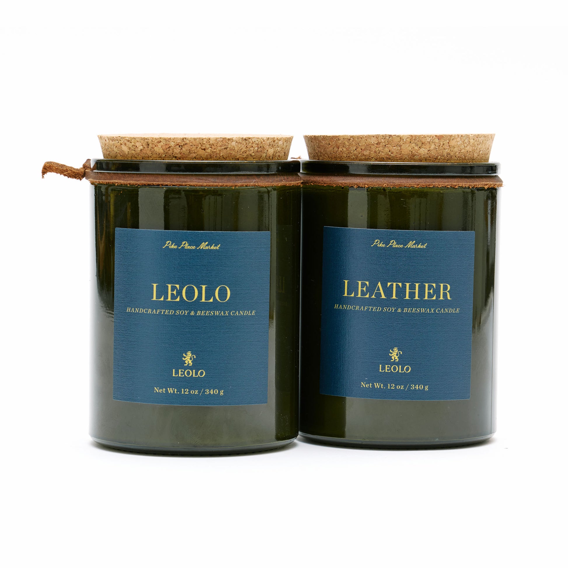 Two candles in green glass jars with cork lists, against white background. 