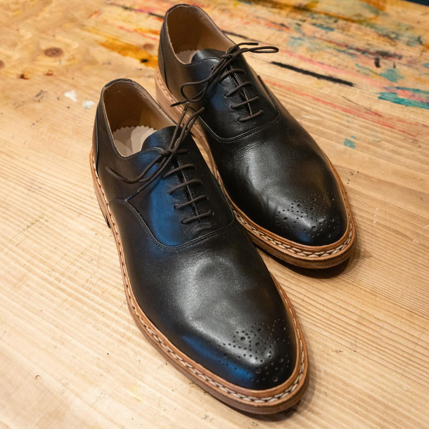 Black leather custom Oxford shoes by Leolo on wood table. 