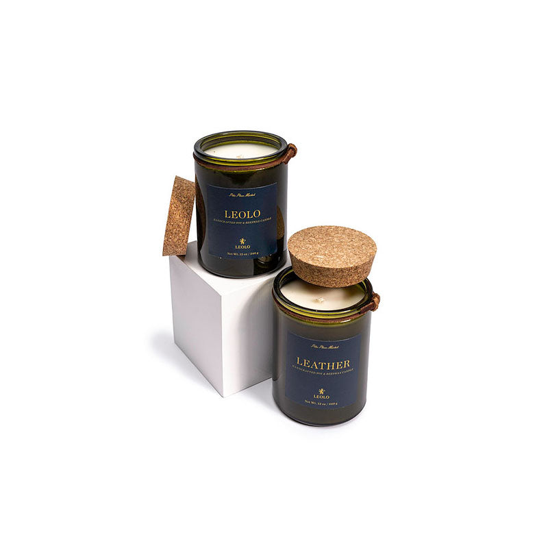 Two candles in green glass jars with cork lists, against white background. 