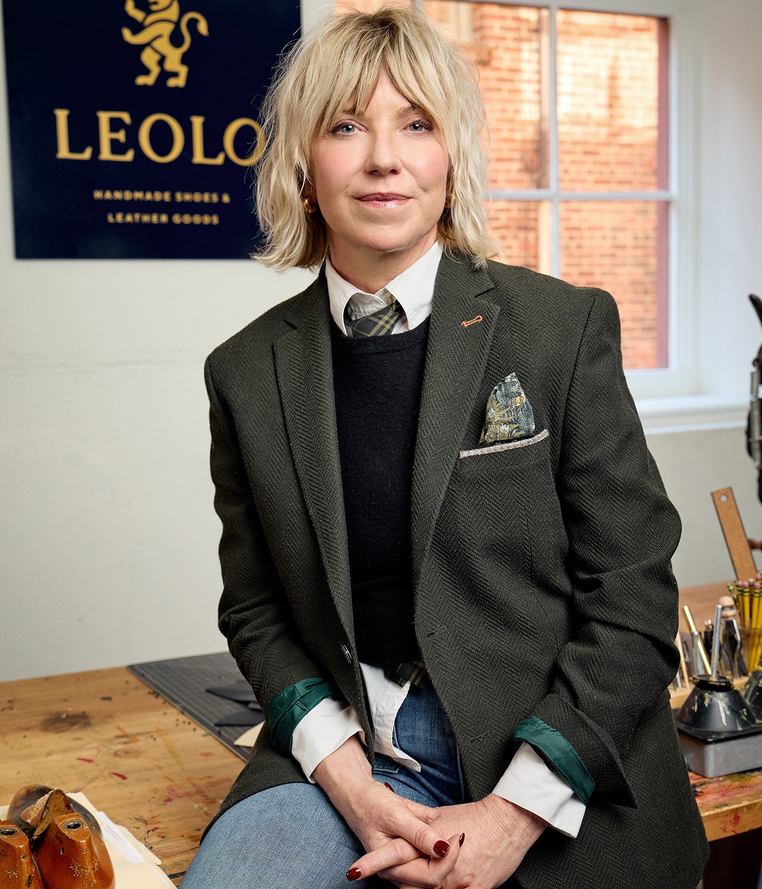 Leolo shoemaker, Leanne, sitting in front of Leolo sign in studio. 