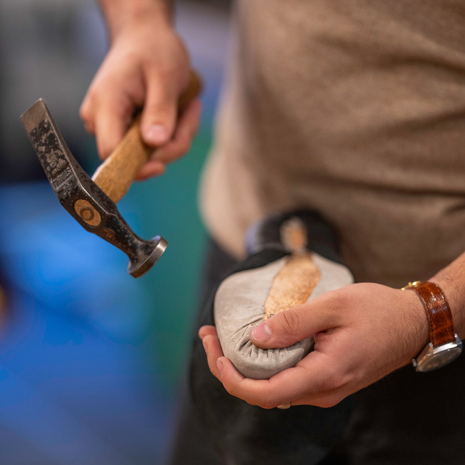 Person holding a shoe-in-progress in one hand and hammer in another. 