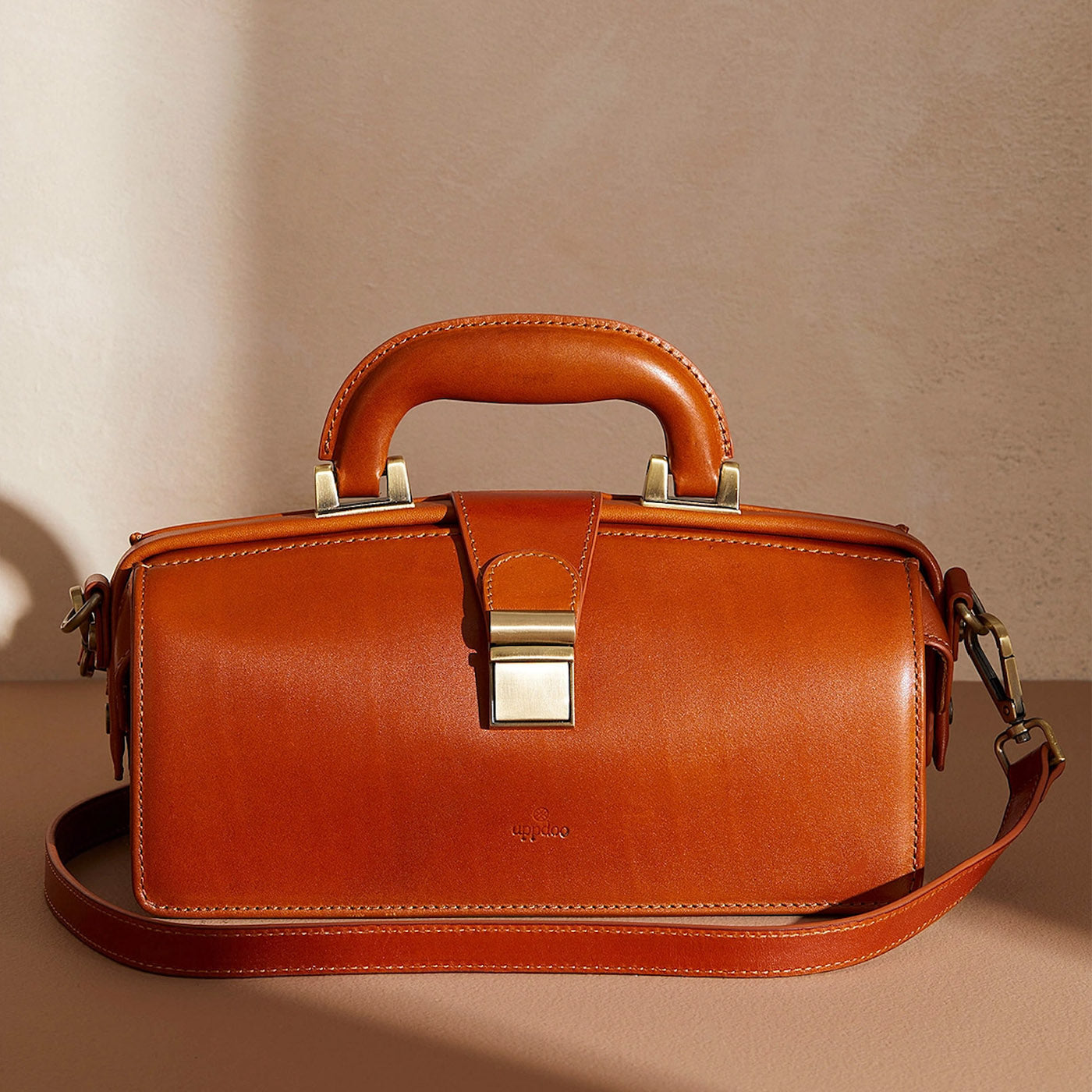 Cognac framed Apex handbag with hinged top by Uppdoo, in front of beige background with shadows. 