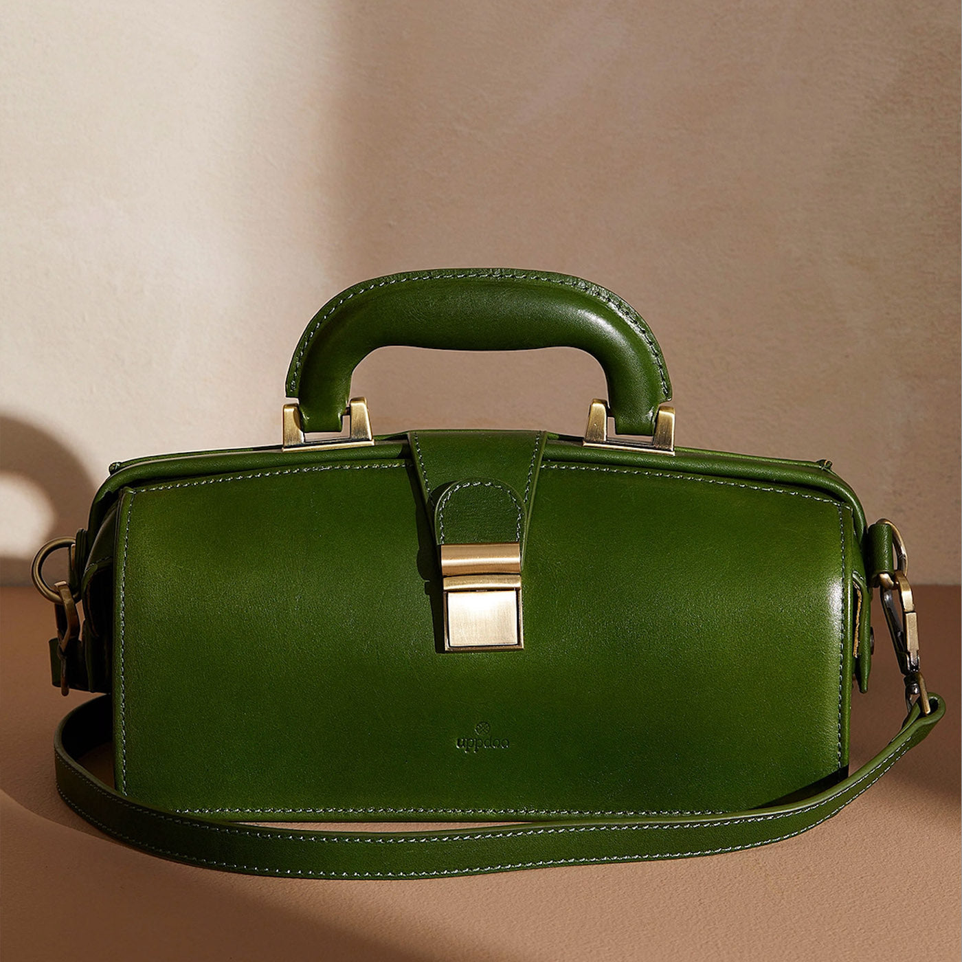 Hunter green framed Apex handbag with hinged top by Uppdoo, in front of beige background with shadows. 