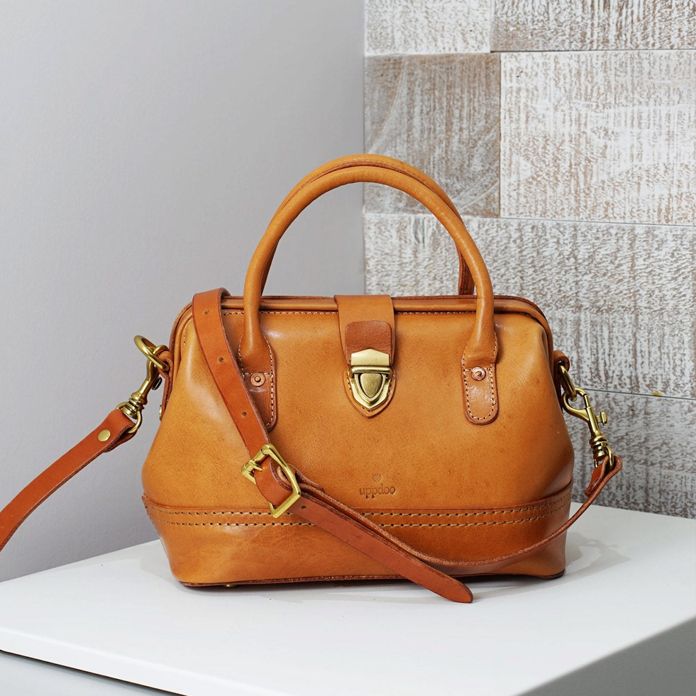 A cognac leather Wonder satchel handbag but Uppdoo on white ledge against grey wall. 