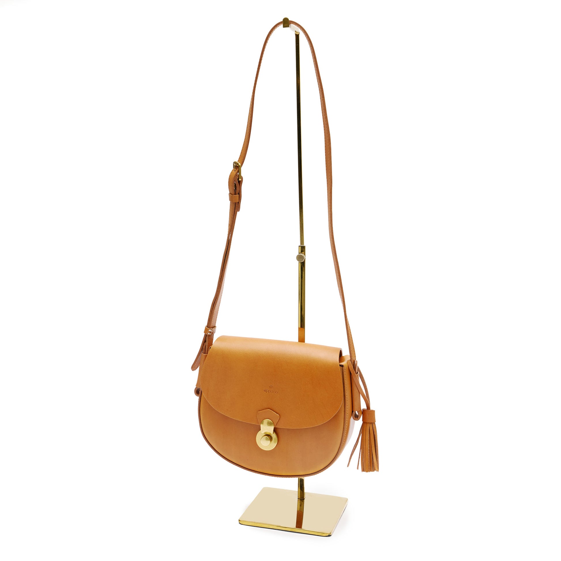 Tan leather handbag with long strap and gold hardware, hanging on bag stand. 